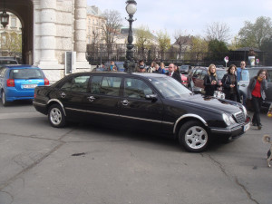 a black limosine making its way outside while surrounded by people